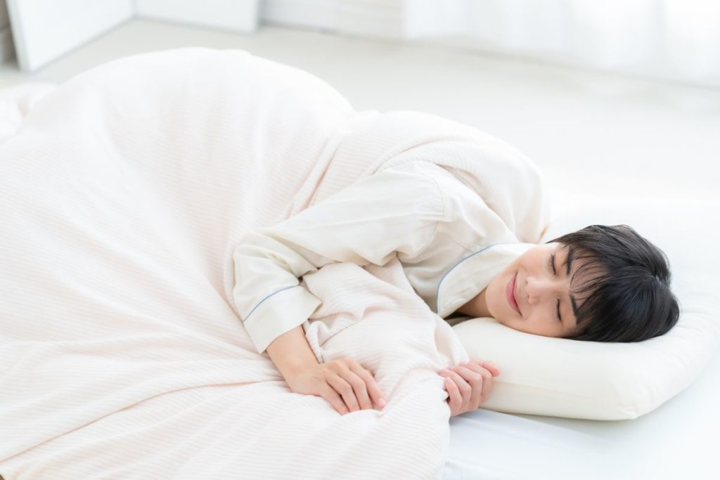 布団にくるまり、気持ちよさそうに眠っている女性のイメージ。