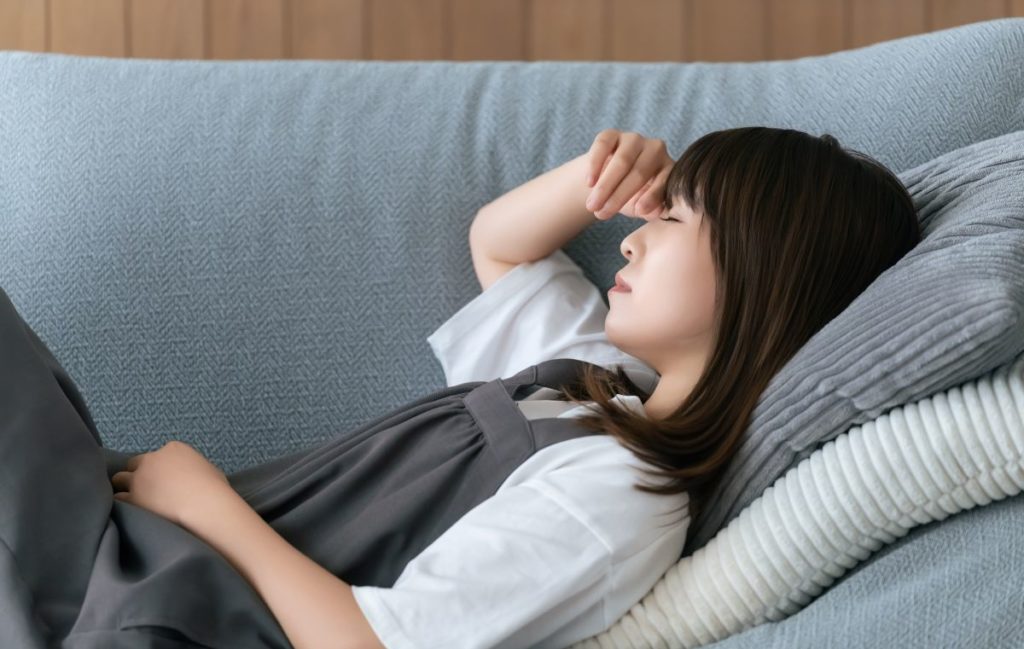 ソファに横になり、体調不良で目元を押さえている女性のイメージ。