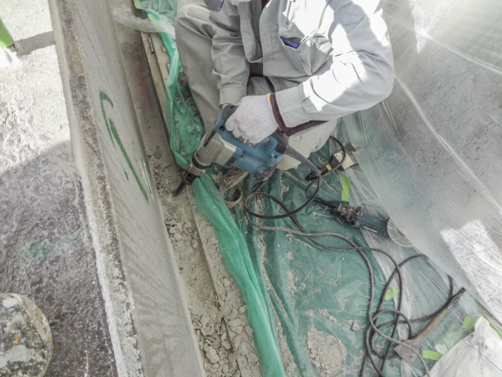 防護シートに囲まれた現場で電動工具を使ってコンクリートを削る作業員。