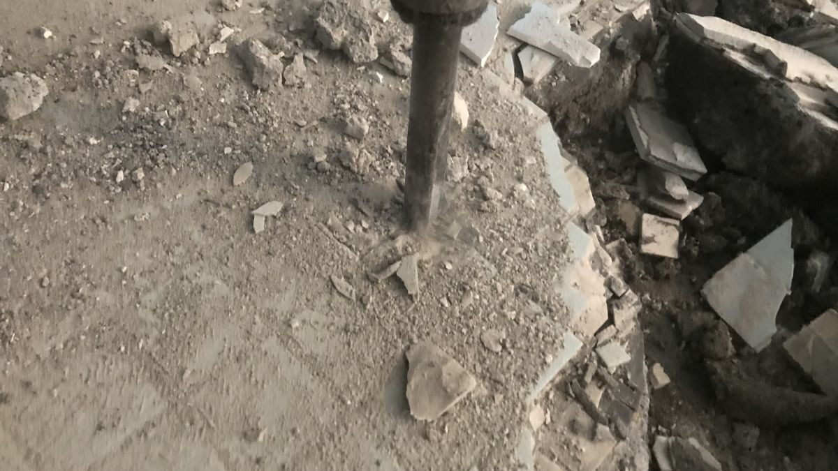 Concrete chipping work on a tiled concrete floor using a power tool, with debris and dust scattered around.