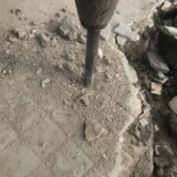 Concrete chipping work on a tiled concrete floor using a power tool, with debris and dust scattered around.