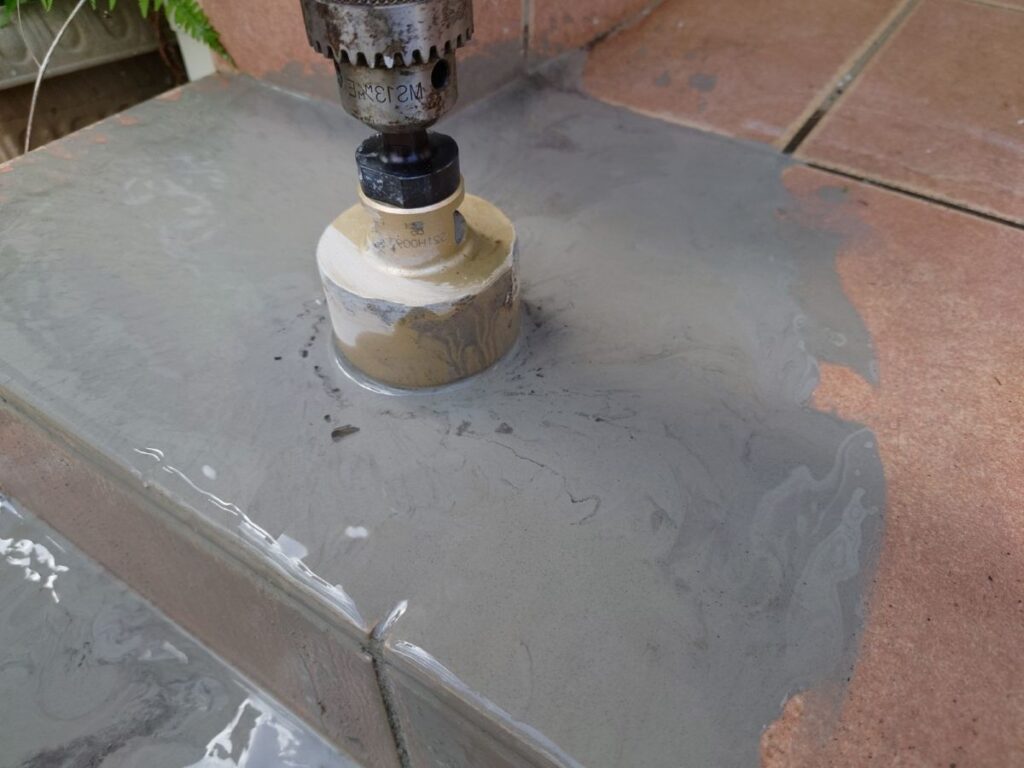 タイル面にコアドリルを使って円形の穴を開ける作業。水を使って粉塵を抑えている。