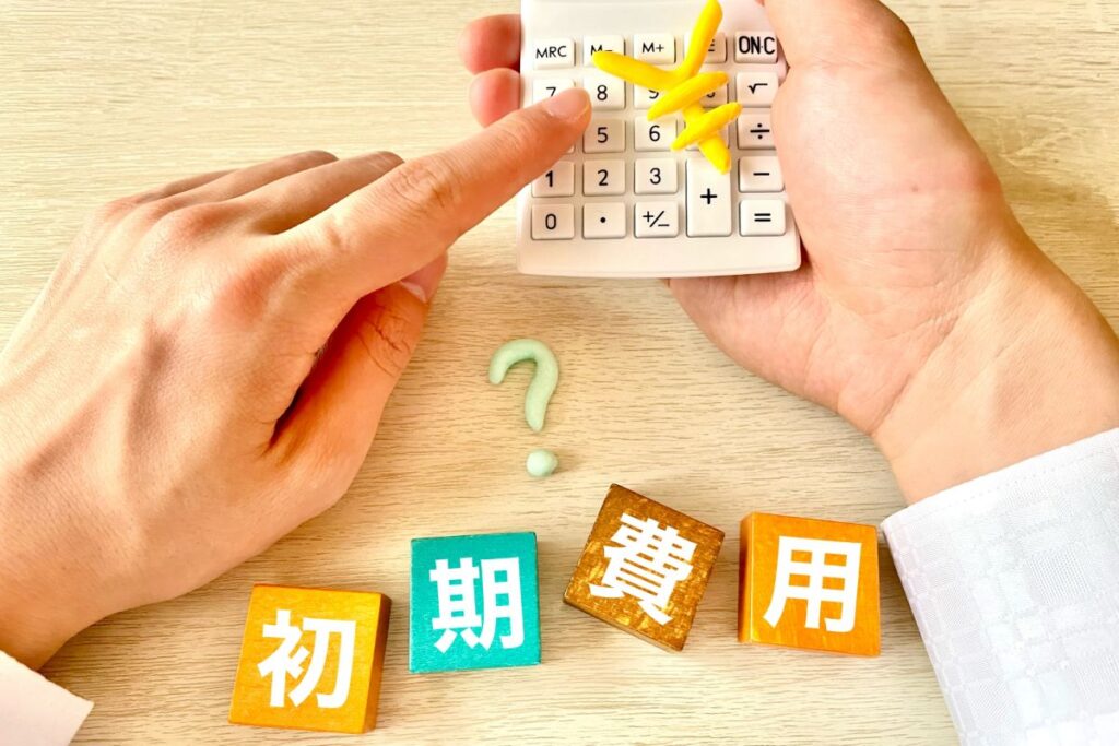 手に持った電卓と「初期費用」の文字ブロック。マンション購入や賃貸にかかる費用を計算しているイメージ。