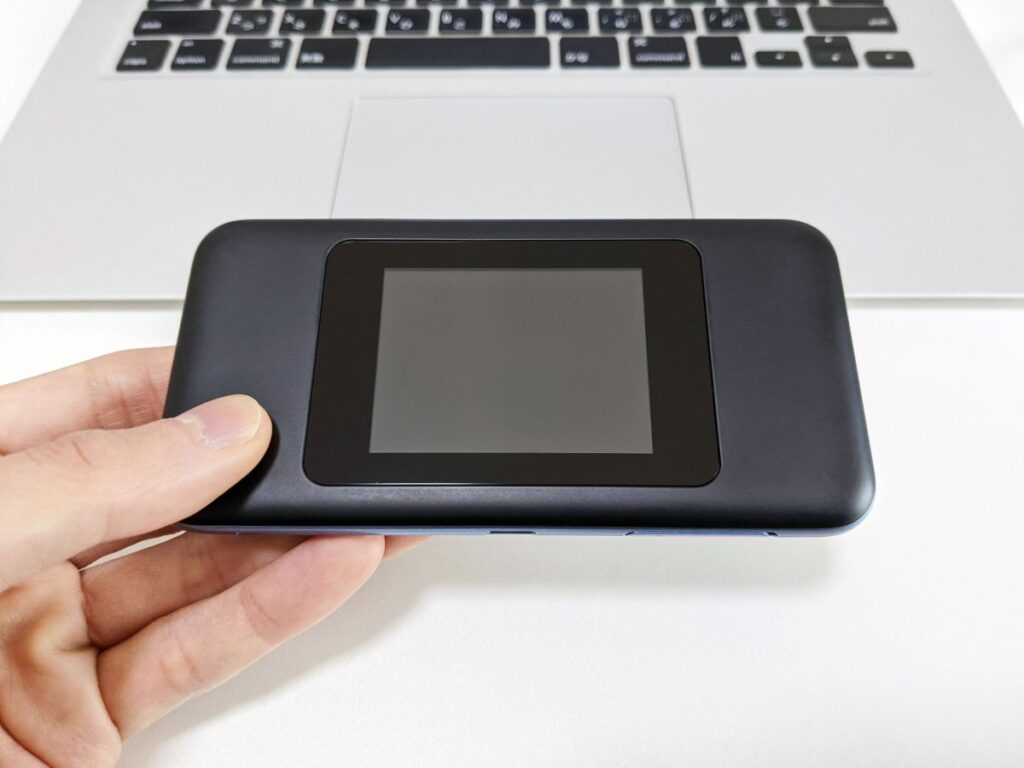 手に持ったモバイルルーターとノートパソコン。一時的なインターネット利用や回線比較の場面。