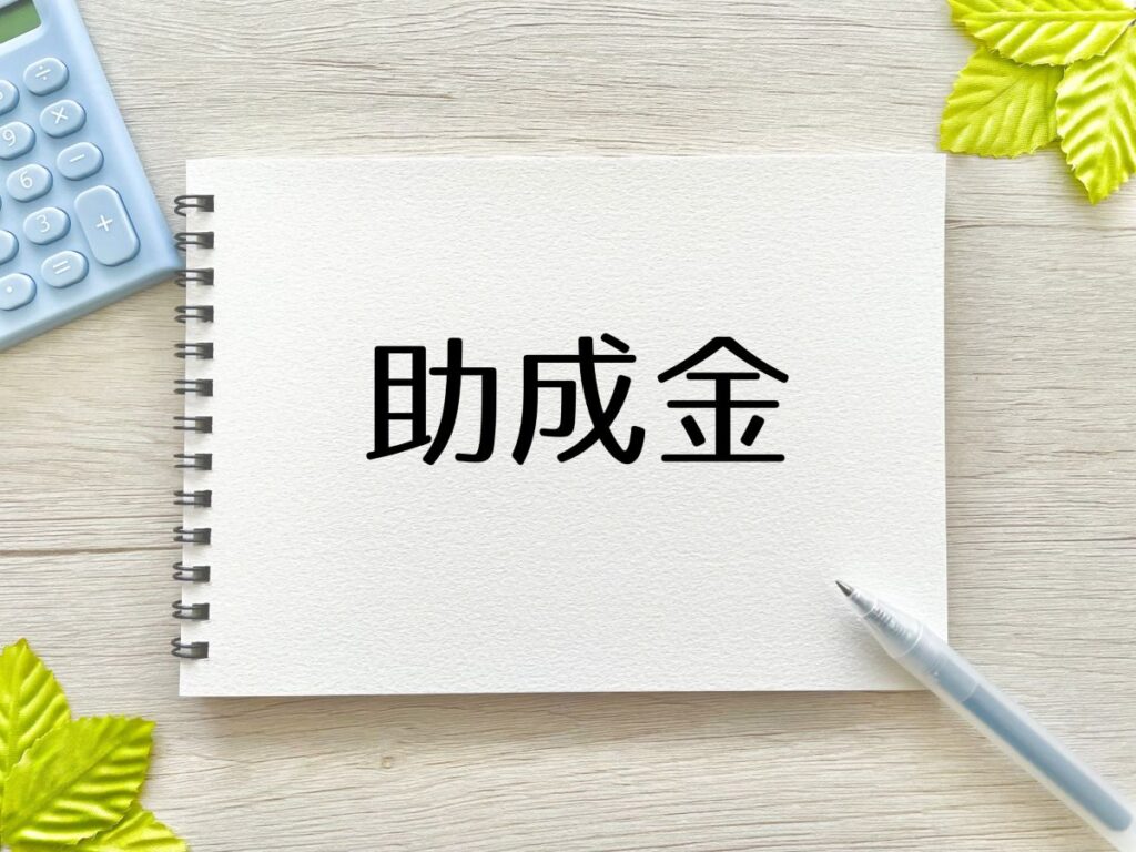 「助成金」と書かれたノートとペン。福祉車両や介護関連の購入費用を支援する補助制度をイメージ。