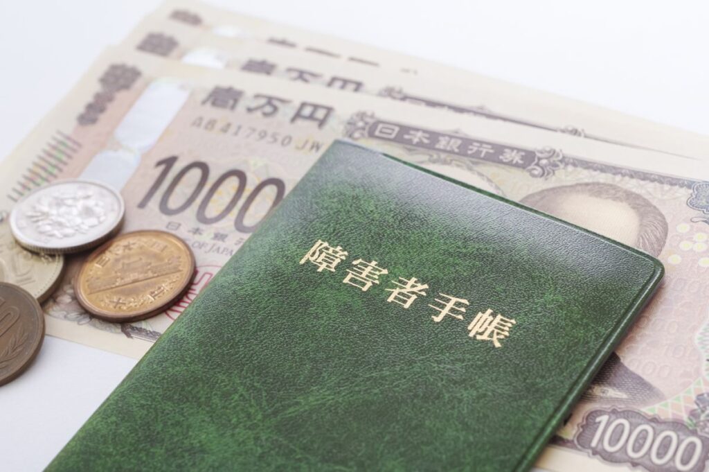 日本の紙幣と硬貨の上に置かれた障害者手帳。障がい者助成制度や経済的支援を象徴する構図。