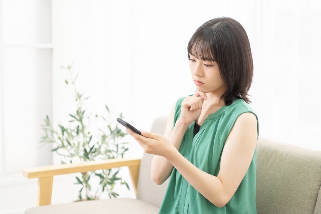 自宅のソファでスマートフォンを見つめ、通信障害情報を確認する女性。インターネット不通時の状況をイメージ。