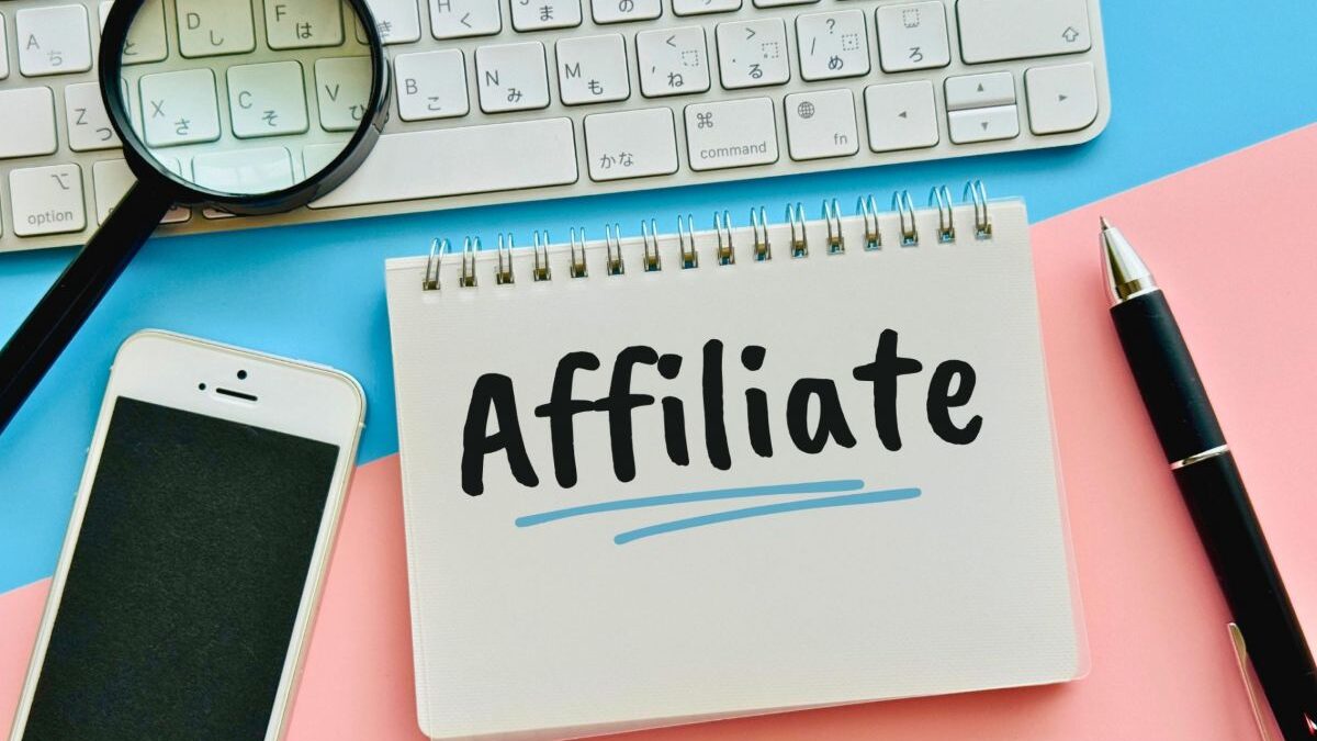 A notebook with "Affiliate" written, placed with a smartphone and keyboard, symbolizing affiliate marketing work and side business.