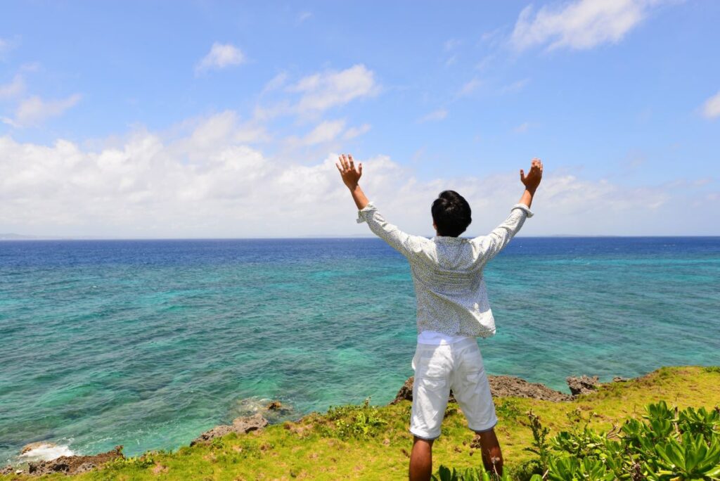 青い海に向かって両手を広げ、メンズVIO脱毛後の快適さや解放感を表現する男性の後ろ姿。