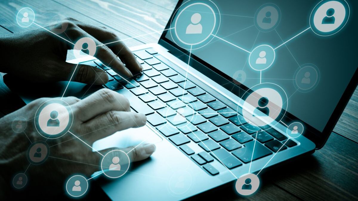 Hands typing on a laptop with network icons of people connected, representing information sharing and networking through social media.