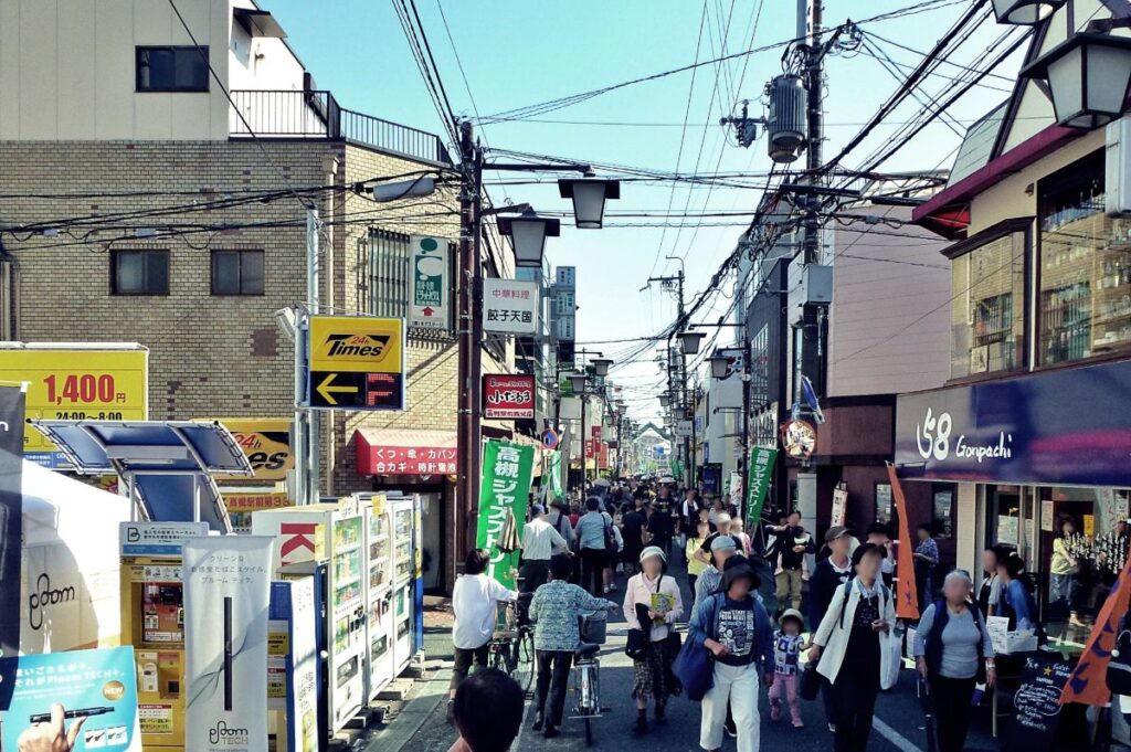 にぎやかな商店街で多くの人々が歩き、地域イベントを楽しんでいる様子。地元の活気と交流を感じる写真。