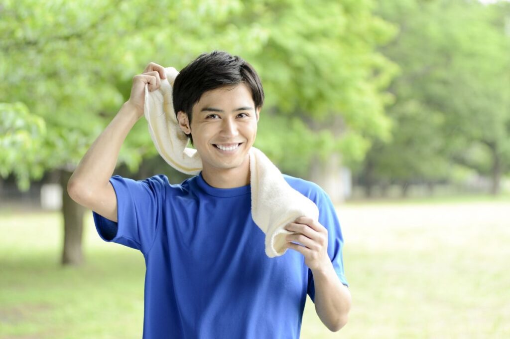 屋外で運動後に笑顔でタオルを首にかける男性。清潔感や爽やかさ、脱毛後の快適さをイメージさせる写真です。