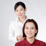 A hairdresser smiling while gently touching a client’s hair, representing trust, skill, and the professional art of creating beauty.