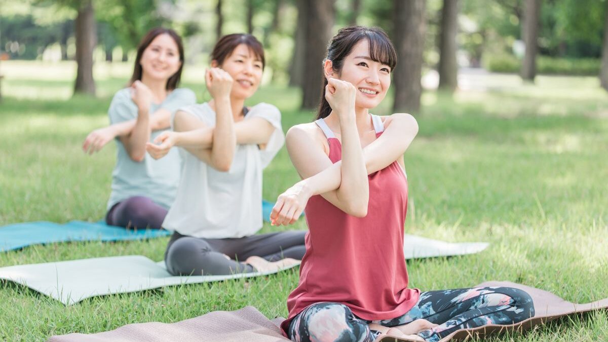 Women participating in a yoga event in the park, smiling as they stretch on the grass, symbolizing mental and physical wellness.