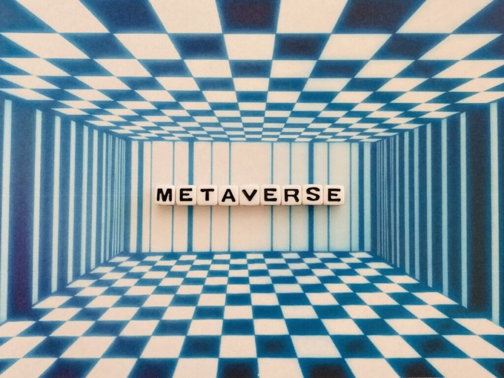 青と白のチェック柄の空間に「METAVERSE」と書かれた文字ブロックが配置された、デジタル世界を象徴するイメージ。