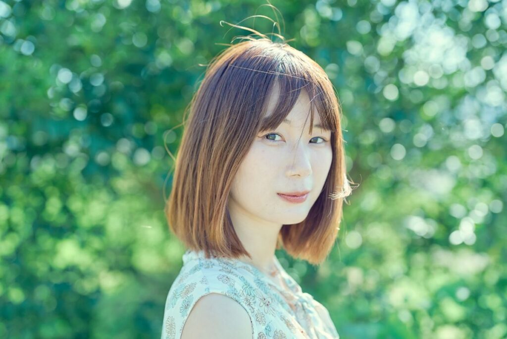 緑の背景の中で柔らかく微笑むボブヘアの女性。ナチュラルで穏やかな雰囲気を感じさせます。