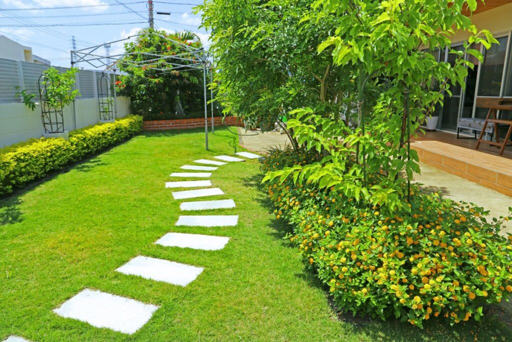 青空の下、芝生と植栽が整えられた明るい庭。白い飛び石が奥へ続いている。