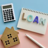 A photo of a house-shaped model, calculator, notebook, and pen, representing the concept of a home loan.