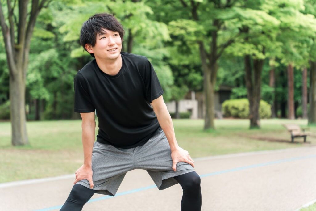 黒いTシャツとグレーのショートパンツを着た男性が公園でストレッチしている。VIO脱毛後も自信を持って体を動かす爽やかな印象の写真。