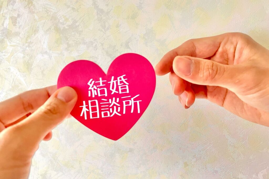 ピンクのハート型カードに「結婚相談所」と書かれ、それを手渡す様子。温かい出会いをサポートするイメージ。