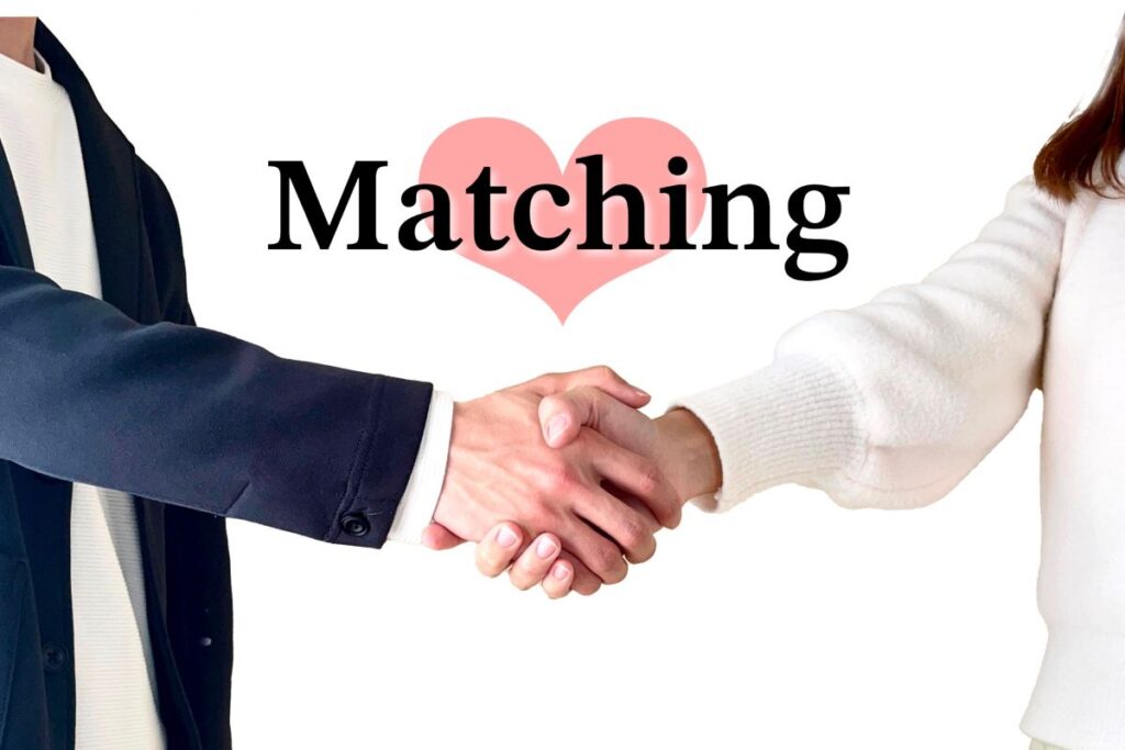 ピンクのハートと「Matching」の文字の前で握手を交わす男女。新しい出会いやご縁を象徴するイメージ。