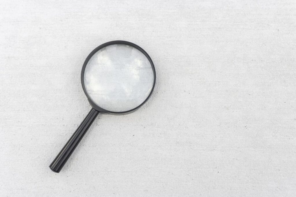 白いコンクリートの上に置かれた黒い拡大鏡の写真。生コンクリートの特徴を調べるイメージ。