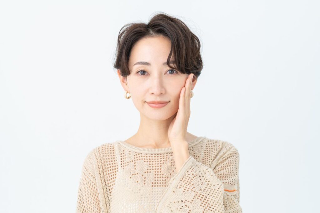 短い髪の女性が手を頬に当てて微笑む姿。上品で落ち着いた大人の女性をイメージさせます。