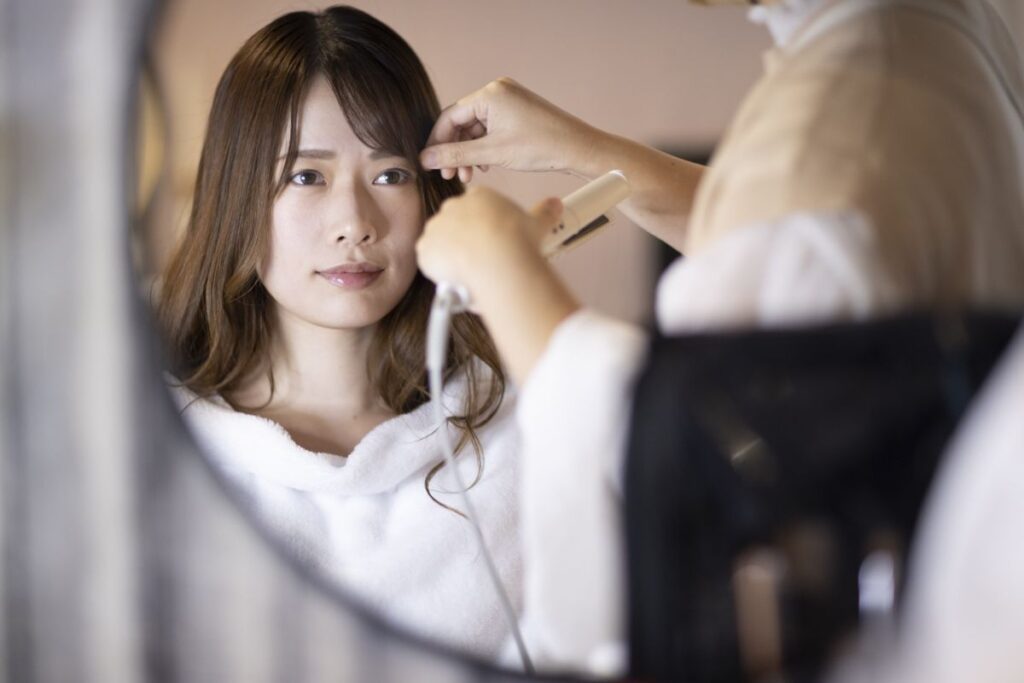 美容室でスタイリストに髪をセットしてもらっている女性。真剣な表情で仕上がりを見つめています。
