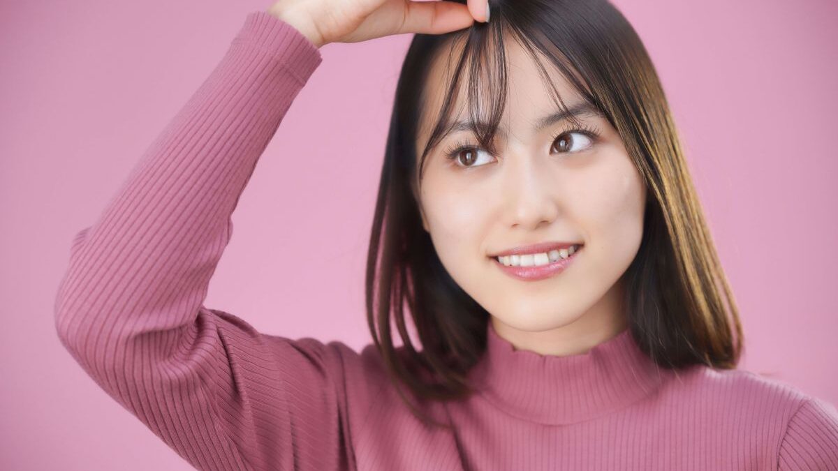 A smiling woman touching her bangs with her fingers, as if checking her hairstyle in the mirror.
