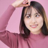 A smiling woman touching her bangs with her fingers, as if checking her hairstyle in the mirror.