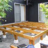 A wooden deck under construction outside a house, showing the frame structure before completion.