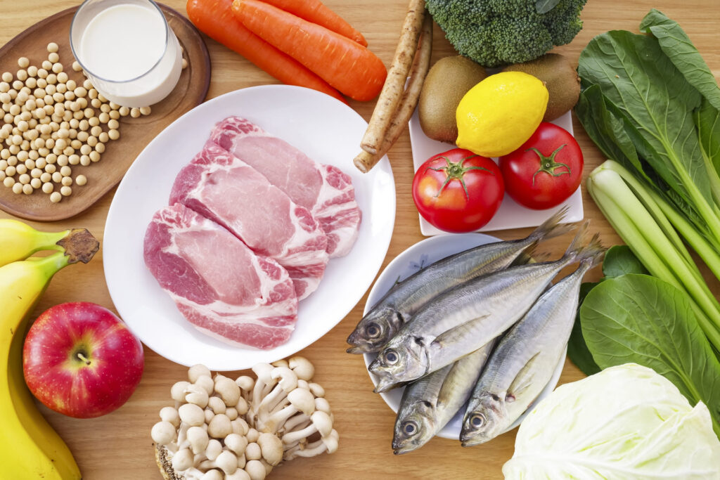 豚肉、魚、大豆製品、緑黄色野菜、果物、きのこ類など、髪の健康に必要なタンパク質やビタミン、ミネラルを豊富に含む食材の集合写真。