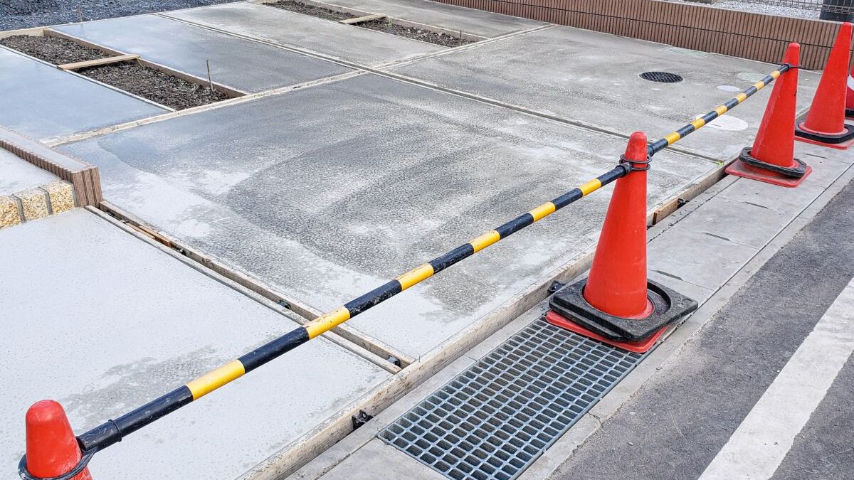 A newly poured concrete driveway under curing, with safety cones placed around the work area.