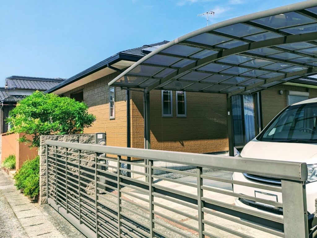 金属フェンスとカーポートを備えた住宅の外観を写した画像。