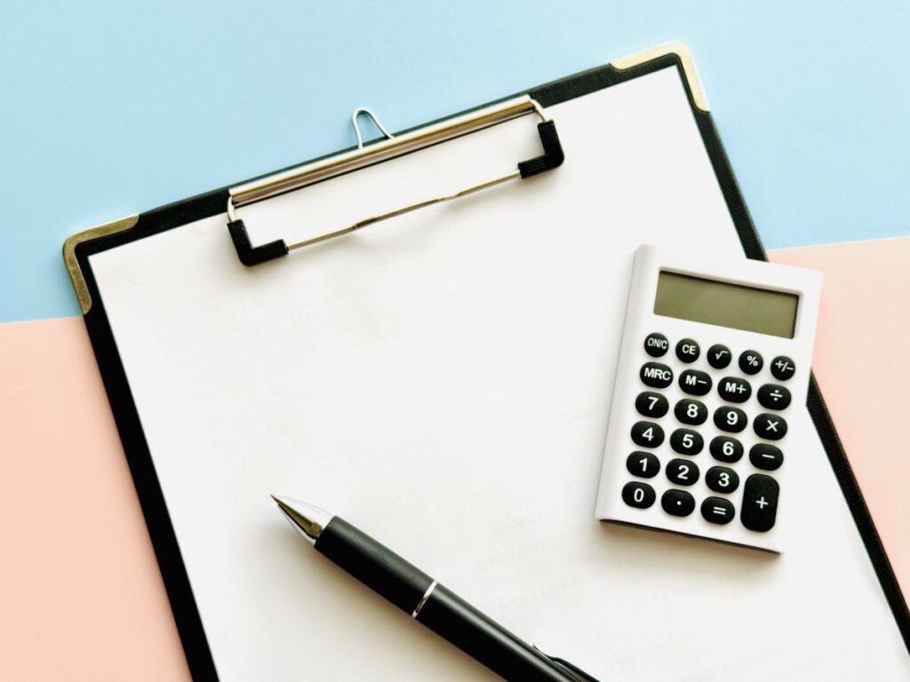 ペット供養にかかる諸費用をイメージさせるように、電卓とメモ用紙、ペンが置かれた画像。