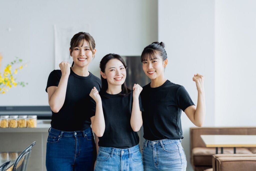 支援の現場で前向きに働く女性スタッフ3名が、感謝の言葉に励まされたように笑顔でガッツポーズをしている様子。