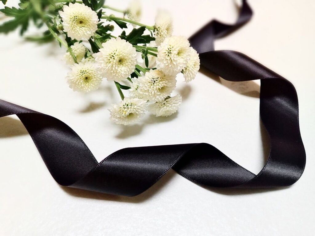 白い菊の花と黒いリボンが並べられ、ペットへのお供えや追悼の気持ちを表すイメージ画像。