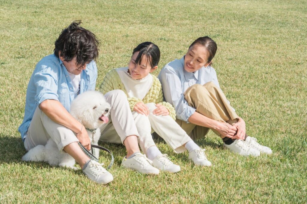 芝生の上で家族がペットの犬と寄り添い、穏やかな時間を過ごしている様子を写した画像。