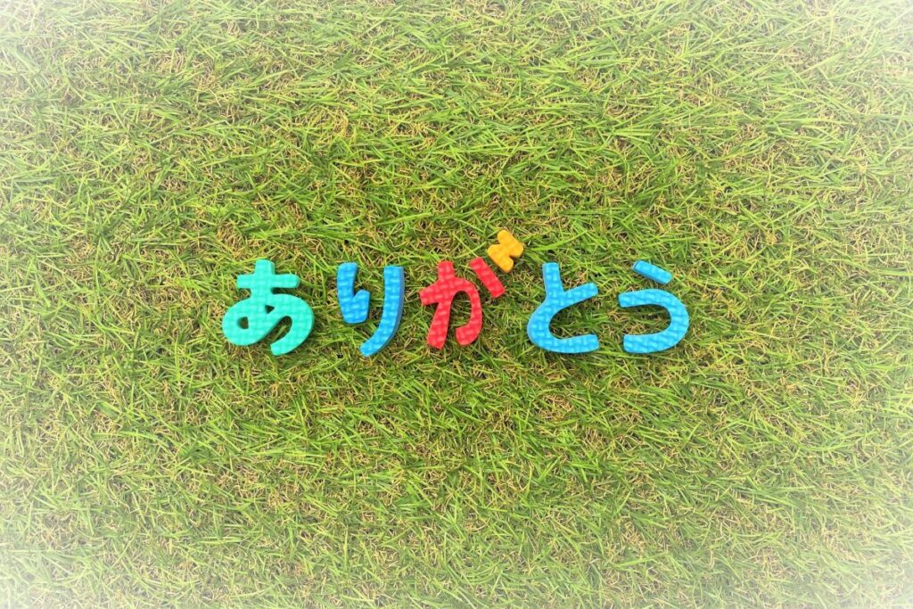 芝生の上にカラフルな文字で並んだ「ありがとう」が、感謝の気持ちの大切さを象徴しているイメージ。