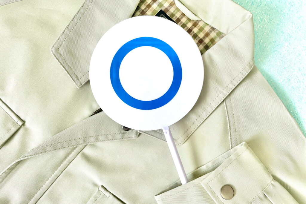 ベージュの作業着の胸元に置かれた、青い丸印(正解・良好を意味する記号)のプレート