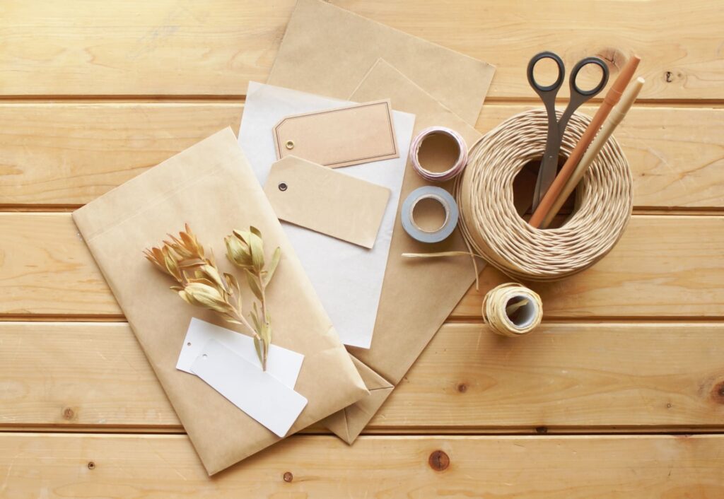 木目調のデスクに置かれた、ネット販売の発送準備風景です。丁寧に台紙へセットされた3種類のハンドメイドピアス（ファー付き、パール、ロングタイプ）が手前に並び、その奥には梱包用の段ボール小箱と、商品を保護するための気泡緩衝材（プチプチ）が用意されています。