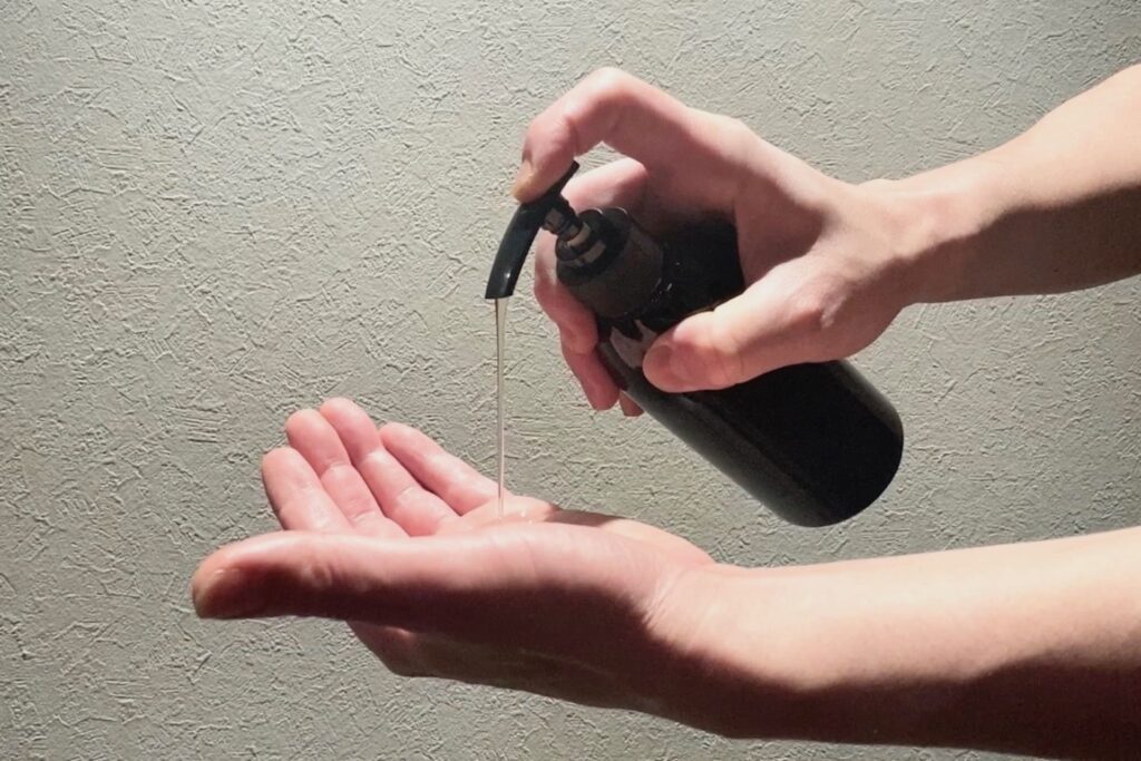 黒いポンプ式のボトルから、手のひらに透明なシャンプー(またはスカルプケア剤)を適量出している様子。正しい洗髪のステップを示すクローズアップ写真。