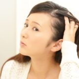 鏡を見ながら自分の髪や頭皮の状態を不安そうにチェックする日本人女性。薄毛、抜け毛、白髪などの髪の悩みを気にする様子