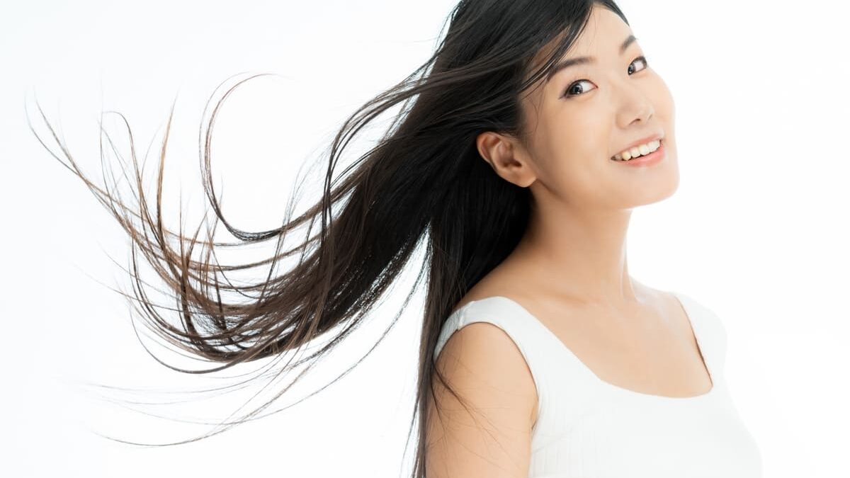 A smiling woman with silky, straight black long hair achieved through hair straightening, fluttering in the wind.