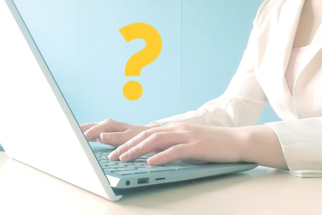 白いノートパソコンでタイピングをする人の手元と、背景に浮かぶ黄色いクエスチョンマーク。ディスプレイ広告とネイティブ広告の選択に迷うユーザーのイメージ。