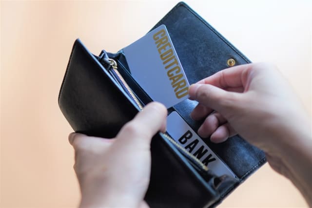 黒のレザー財布からクレジットカードを取り出す手元の写真。日常使いの利便性をイメージ。