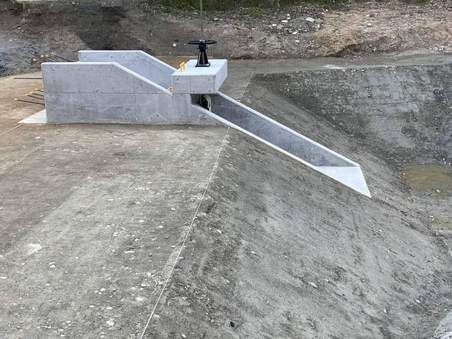 建築現場におけるコンクリート製水門の施工完了写真。手前の斜面（のり面）もコンクリートで覆われている。