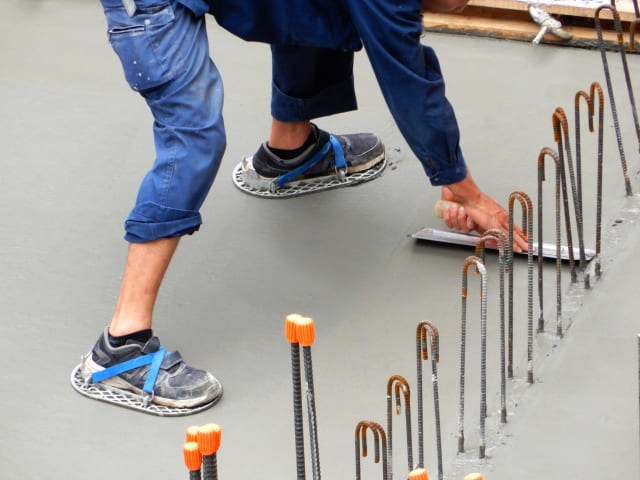 建設現場にて、土間スパイクを履き金コテでコンクリート表面を平滑に仕上げる左官職人