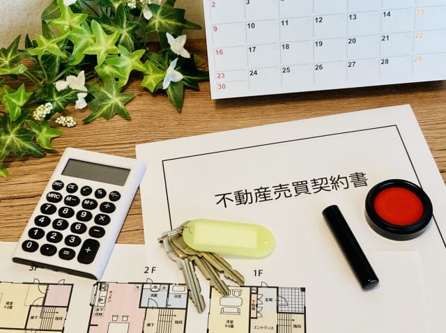 デスクに置かれた不動産売買契約書と家の鍵、電卓、図面の俯瞰写真