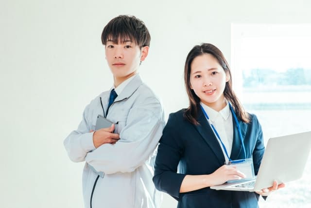 Image of cooperation between a construction company site manager in workwear with a tablet and a prime contractor representative in a suit with a laptop.